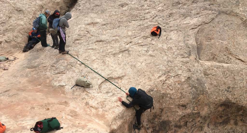 A person wearing safety gear is secured by a rope as they rappel into a canyon. 